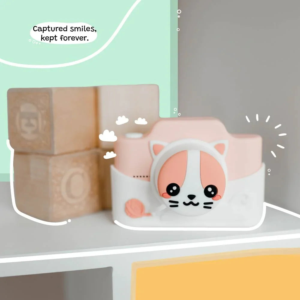 kiimento Meowie the Cat digital camera with pink silicone cover displayed on a shelf beside wooden toy blocks, capturing a playful and cute design.